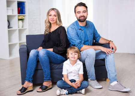 happy family portrait - couple and little son sitting on sofa in living roomの写真素材