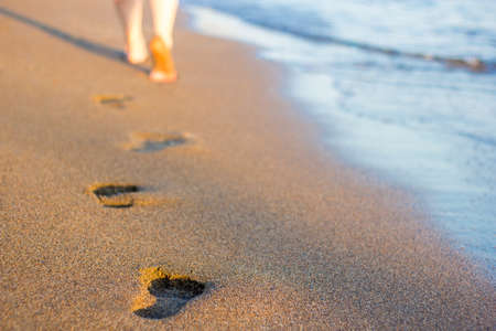 summer end - close up of female legs and footprints on the sunset beach in warm countryの写真素材