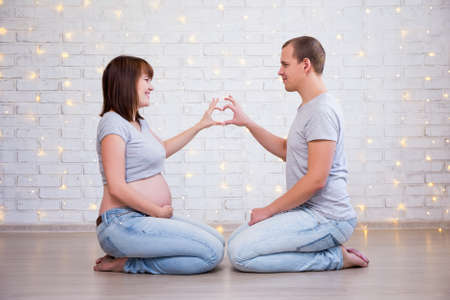 happy pregnant couple making a heart shape with their handsの写真素材