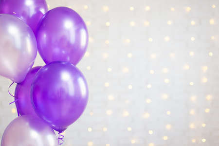 birthday party concept - purple air balloons over white brick wall background with lightsの写真素材