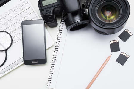 photographer's workplace - camera, photography equipment, laptop, smart phone and notepad with pen over white tableの写真素材