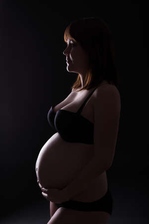 silhouette of pregnant woman in lingerie over black backgroundの写真素材
