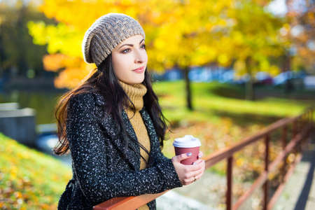 portrait of young woman drinking coffee in yellow autumn parkの写真素材