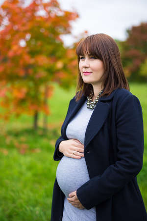 portrait of dreaming pregnant woman posing in autumn parkの写真素材