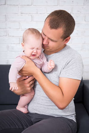 portrait of crying baby girl on father's hands at home