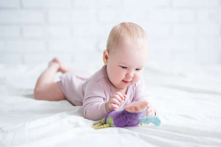 portrait of little baby lying on the bed with toy at homeの写真素材