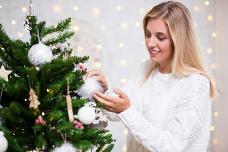 portrait of young woman decorating Christmas tree at homeの写真素材
