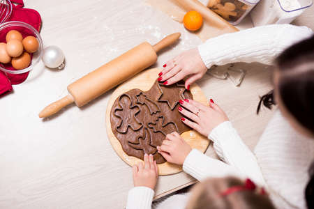 top view of little girl and her mother cooking Christmas cookies or gingerbreads in kitchen