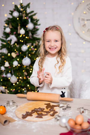 portrait of cute little girl making Christmas cookies in kitchen with Christmas treeの写真素材