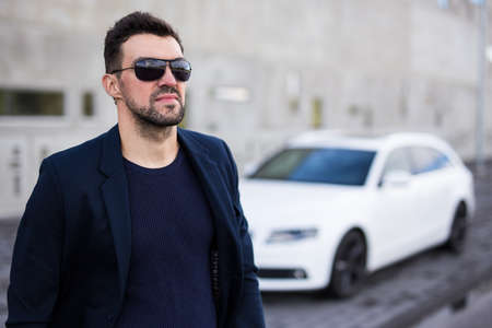 handsome business man in sunglasses posing with his white car