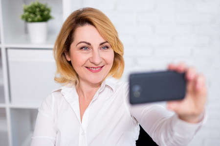 portrait of cheerful mature business woman taking selfie photo with smart phoneの写真素材