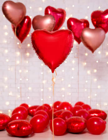 Valentine's day background - group of red heart shaped foil balloons over white brick wallの写真素材