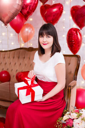 valentine's day concept - young woman with gift box and red heart-shaped air balloonsの写真素材
