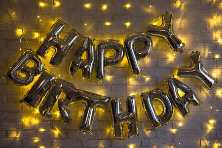 birthday party decoration - happy birthday letters air balloons over brick wall with lights in dark roomの写真素材