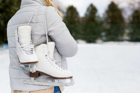 back view of woman holding ice skates at rink in winter parkの写真素材