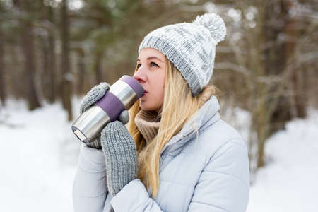 portrait of young beautiful blond woman drinking coffee in winter park or forestの写真素材