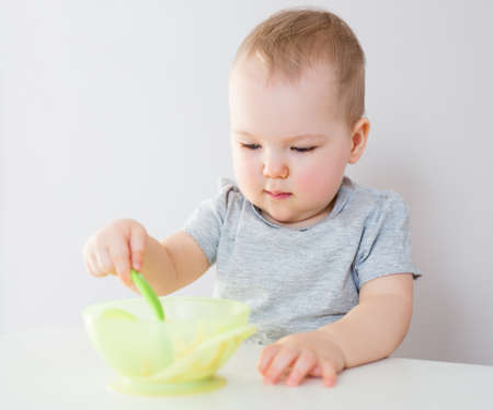 portrait of cute baby girl eating porridge with plastic spoonの写真素材