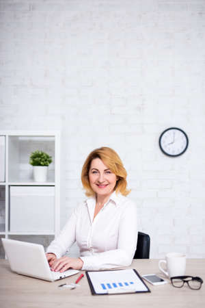 portrait of mature business woman working in office and copy space over white brick wallの写真素材