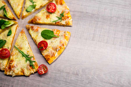 close up top view of tasty sliced pizza with tomatoes and herbs over wooden table background with...