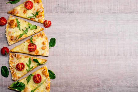 slices of tasty pizza with tomatoes and herbs over wooden table background with copy space