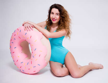 young beautiful sexy woman in swimsuit posing with giant donut over gray backgroundの写真素材