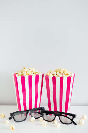 cinema concept - two red striped boxes with popcorn and 3d glasses with copy space over white wall...