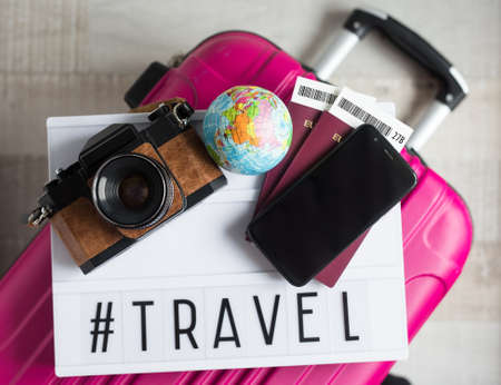 travel and vacation concept - suitcase, passports, tickets, globe, smart phone, vintage camera and lightbox with travel hashtagの写真素材