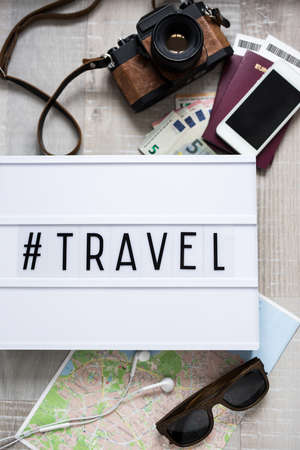 travel concept - close up of travel objects and and lightbox with travel hashtag over wooden table backgroundの写真素材