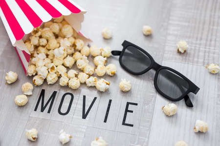 cinema concept - close up of 3d glasses and popcorn with movie word on wooden background