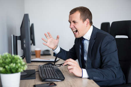 portrait of angry stressed businessman screaming on his computer in modern officeの写真素材