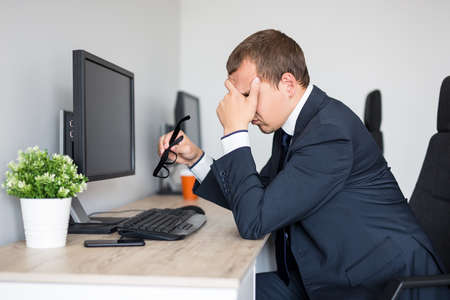 tired young businessman with problems and stress sitting in modern office