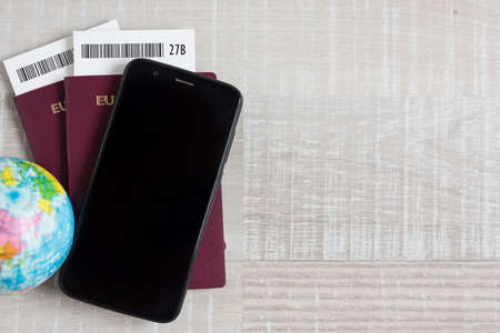 travel and vacation concept - close up of passports, tickets, little globe, smart phone and copy space over wooden table backgroundの写真素材