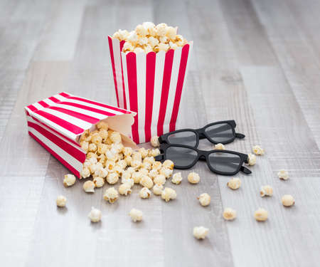 cinema concept - close up of 3d glasses and popcorn in striped boxes on wooden table background