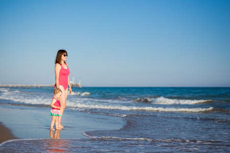 summer vacation and travel concept - portrait of happy mother with little daughter in pink swimsuits at the beachの写真素材