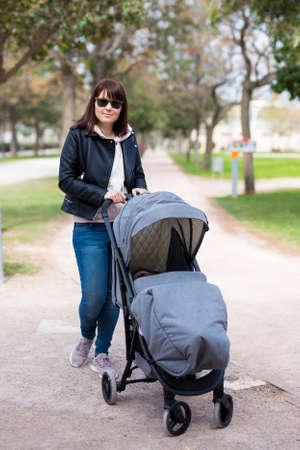 portrait of young mother walking with baby carriage in spring park