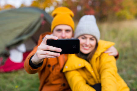 travel, love and autumn concept - happy couple in love taking selfie photo with smart phone in autumn forestの写真素材