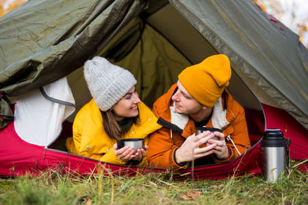 travel, trekking and hiking concept - portrait of couple drinking tea in green tentの写真素材