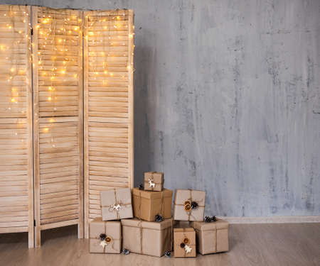 heap of christmas gifts and folding screen with lights - copy space over concrete grey wall...