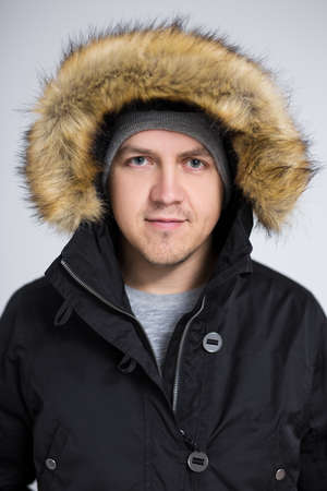 close up portrait of young handsome man in warm winter jacket over gray background