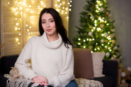 christmas and new year concept - young woman sitting in decorated living room with Christmas tree...