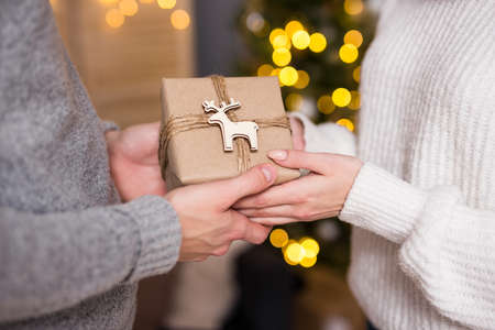 christmas, new year and love concept - close up of man giving gift box to his girlfriend in decorated room with garland and Christmas treeの写真素材