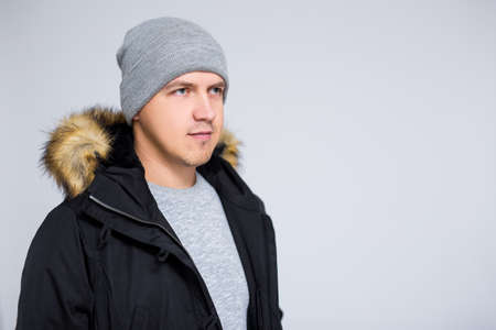 portrait of young man in warm winter clothes posing over gray backgroundの写真素材