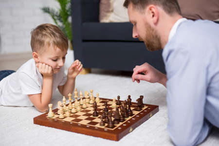 young father and little son lying on floor at home and playing chessの写真素材