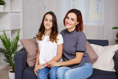 family and love concept - smiling mother and daughter sitting in living roomの写真素材