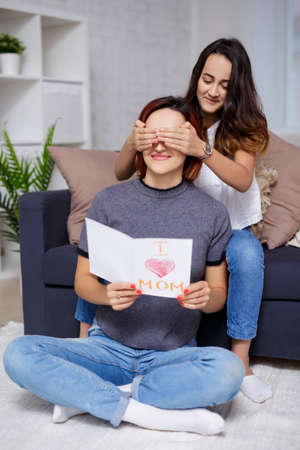 family and love concept - daughter giving handmade greeting card to her mother in living room
