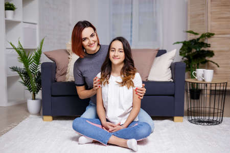 family and home concept - portrait of smiling mother and daughter sitting in living roomの写真素材