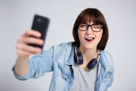 portrait of funny young woman or teenage girl taking selfie photo with smartphone over gray backgroundの写真素材