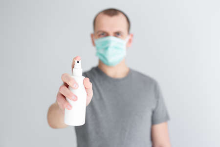coronavirus protection and disinfection concept - man in medical mask spraying sanitizer spray over...