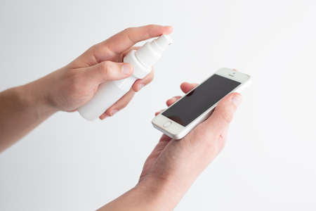 coronavirus protection and disinfection concept - man cleaning or disinfecting smart phone screen with sanitizer sprayの写真素材