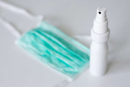 medicine, health care, pandemic and hygiene concept - spray sanitizer and protective mask over white...